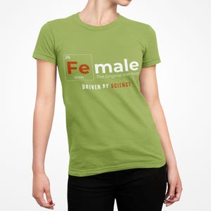 Puede incluir: Una camiseta verde con un gr&aacute;fico blanco de un elemento de la tabla peri&oacute;dica. El elemento est&aacute; etiquetado como "Fe" para el hierro y "Female" con el texto "The Original Iron Man" y "Driven by Science".