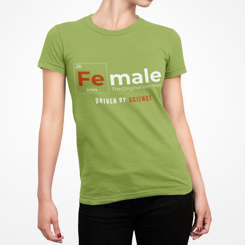 Puede incluir: Una camiseta verde con un gr&aacute;fico blanco de un elemento de la tabla peri&oacute;dica. El elemento est&aacute; etiquetado como "Fe" para el hierro y "Female" con el texto "The Original Iron Man" y "Driven by Science".