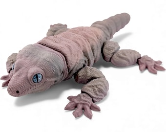 May include: A articulated lizard figurine with a textured, dusty pink body and prominent, light blue eyes. The reptile features segmented joints along its back and limbs, allowing for a flexible, realistic pose with detailed skin scales.