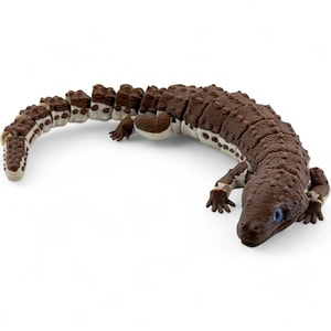 May include: An articulated lizard figurine featuring a textured brown back with a bumpy surface and a smooth cream-colored underside. The creature has four legs, a long segmented tail, and bright blue eyes, designed with a flexible, jointed body.