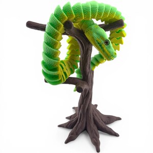 May include: A segmented, articulated snake figure with a vibrant green and yellow gradient pattern, coiled around a brown, textured tree branch stand. The snake features a detailed head with visible eyes and nostrils, resting on the dark brown base.