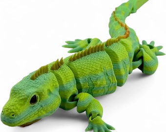 May include: A 3D printed articulated lizard figurine featuring a vibrant green and yellow striped pattern. The reptile has a textured skin surface, a row of small spikes along its back, and a segmented body design that allows for movement.