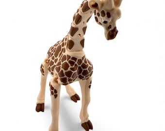 May include: A posable giraffe figurine featuring a cream-colored body with distinct brown patches. The articulated toy has a long neck, small ossicones on the head, and dark brown hooves, designed with visible joints for movement and posing.