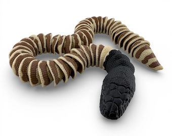 May include: A segmented articulated snake toy featuring a solid black head with a textured scale pattern. The body consists of alternating brown and cream-colored curved segments that create a flexible, winding form across the surface.