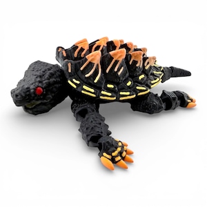 May include: A black turtle figurine with a textured shell featuring orange spikes and yellow accents. The creature has bright red eyes, articulated limbs, and orange claws on its feet. The design includes a pointed tail and a detailed head.