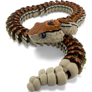May include: An articulated snake figurine featuring a segmented body with a color palette of cream, burnt orange, and black. The head displays detailed scale textures, a black marking on the crown, and light blue eyes, with a rattle at the tail end.