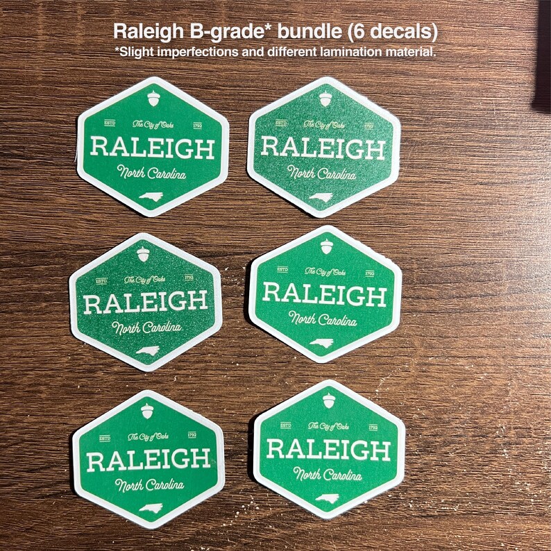 Pu&ograve; includere: Un pacchetto di sei adesivi esagonali verdi con il testo Raleigh North Carolina, The City of Oaks e una piccola icona di ghianda. Il testo Raleigh B-grade bundle (6 decals) *Slight imperfections and different lamination material &egrave; visibile.