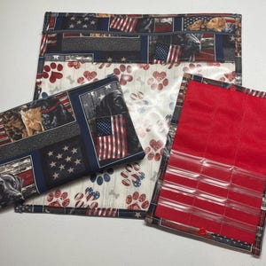 May include: Three fabric pouches with a patriotic theme. The largest pouch is clear with a white background and paw prints. The medium pouch has a blue and red background with stars and stripes and images of dogs. The smallest pouch is red with clear plastic pockets.