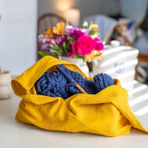 May include: A yellow fabric bag with a blue knitted ball of yarn and knitting needles inside.