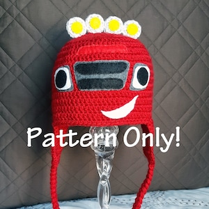 May include: Red crochet hat with a car design, featuring a white smile, black eyes, and yellow lights on top. The hat has long ties and the text "Pattern Only!" is visible below the hat.