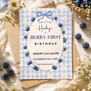 May include: A light blue gingham patterned invitation with the text "Hailey's Berry First Birthday". The invitation is decorated with blueberries and daisies. A basket of blueberries and flowers are in the background.