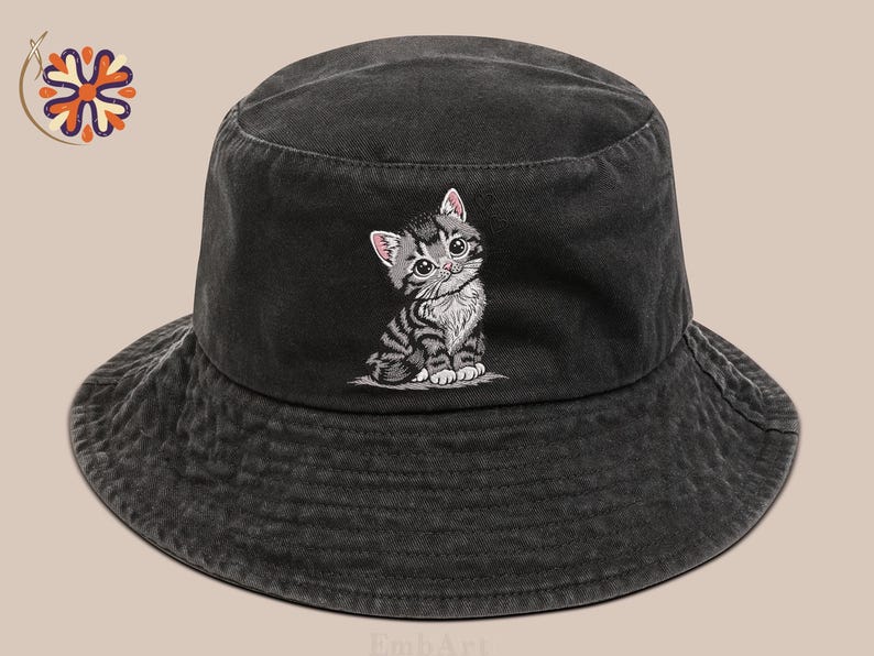 May include: A dark grey bucket hat featuring an embroidered kitten design. The kitten is grey and white with pink ears. The hat is made of a soft, textured material, suitable for casual wear.