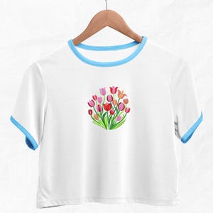 May include: White cropped t-shirt with a blue trim around the neckline. The shirt features an embroidered design of a bouquet of pink, red, and orange tulips.
