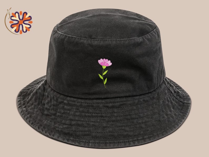 May include: Black bucket hat with a pink flower embroidery. The hat features a wide brim and a simple, casual design. The flower has pink petals and a green stem and leaves. The hat is made of a soft, textured fabric.