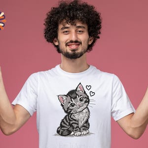 May include: White t-shirt with a detailed illustration of a grey and black tabby kitten with large eyes and two hearts. The kitten is sitting, and the design is centered on the shirt.