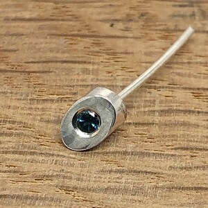 May include: A silver earring with a blue gemstone set in an oval-shaped setting.