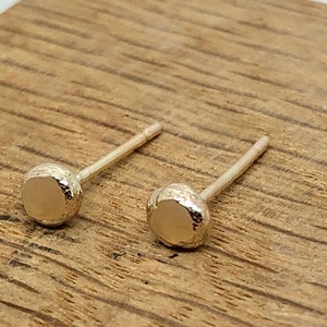 May include: A pair of small, round, silver stud earrings with a textured surface.