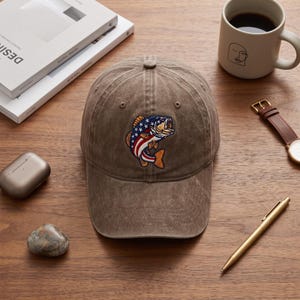 May include: A brown, distressed-finish baseball cap featuring an embroidered patch of a fish with a red, white, and blue American flag pattern on its body. The cap has a structured crown, a curved brim, and a button on the top centre.