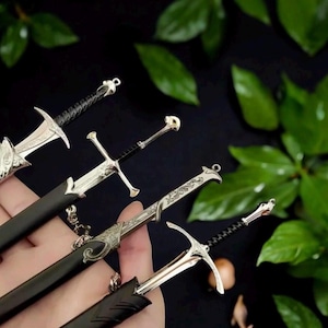 May include: Miniature silver swords with black sheaths. The swords have intricate designs on the hilts and blades. The image is set against a dark background with green leaves, creating a fantasy theme.