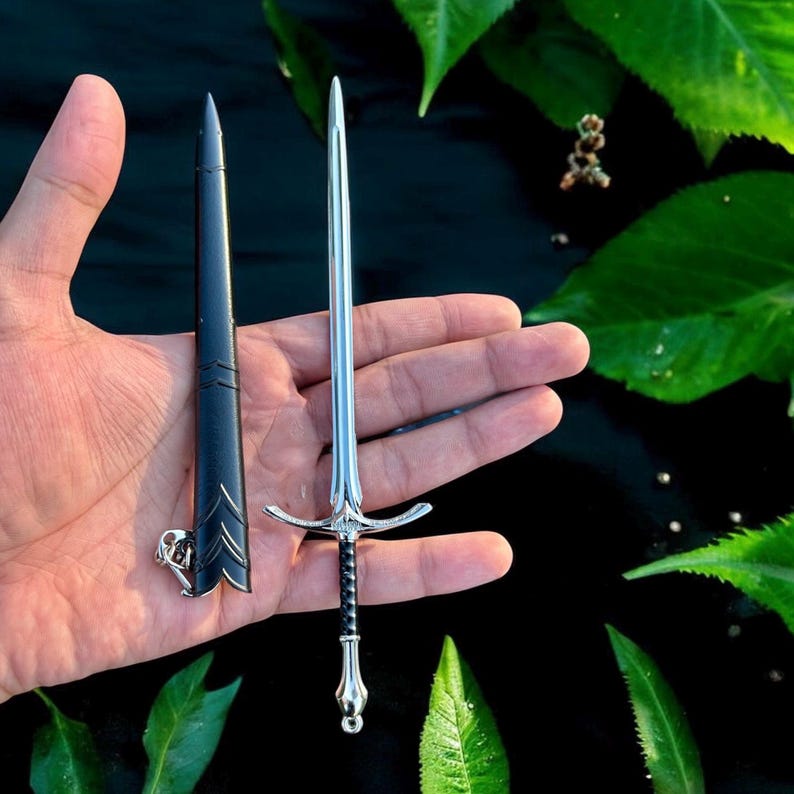 Puede incluir: Una espada plateada en miniatura con empu&ntilde;adura negra y vaina a juego. La espada presenta una guarda detallada y una hoja afilada. La vaina tiene grabados decorativos. La espada mide unos 15 cm de largo.