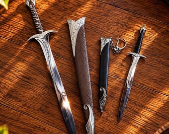 Puede incluir: Una espada plateada con una empuñadura intrincada y una vaina texturizada marrón a juego, junto a una daga plateada más pequeña con mango negro, funda negra y una anilla de llavero metálica en la parte superior.