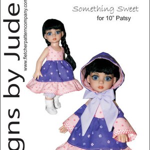 以下が含まれることがあります： 白い水玉模様の紫とピンクのドレスを着た2体のドール。左側のドールはピンクのフリルが付いた紫のドレスを着ており、右側のドールはピンクのフリルが付いた紫のドレスとラベンダー色のフード付きジャケットを着ています。ドールの上には「Something Sweet for 10" Patsy」という文字があります。