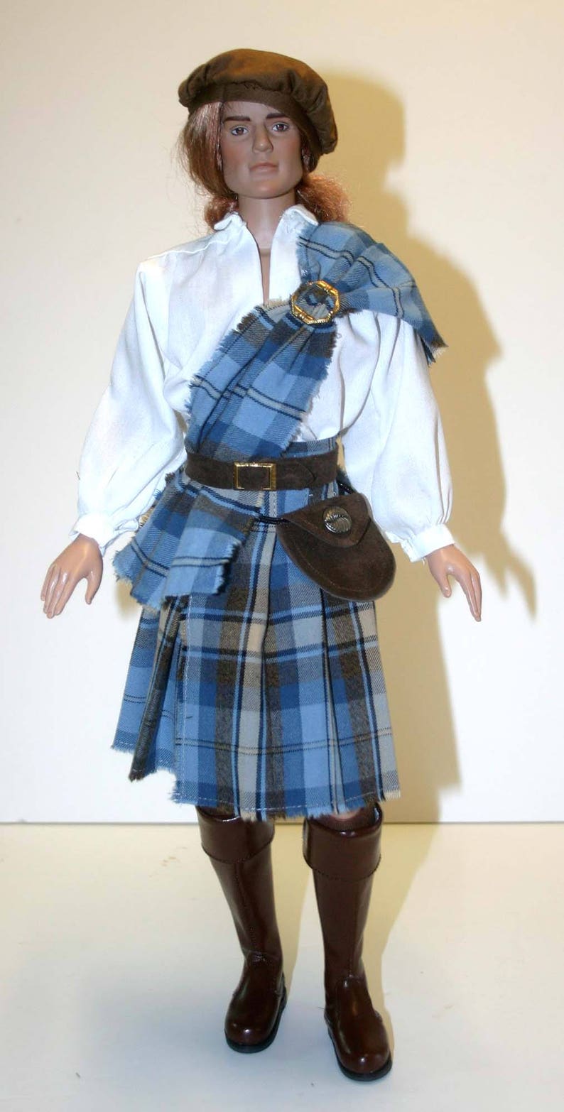 May include: A doll wearing a brown hat, a white shirt, a blue and brown plaid kilt, a brown leather belt with a silver buckle, a brown leather pouch with a silver button, and brown leather boots.