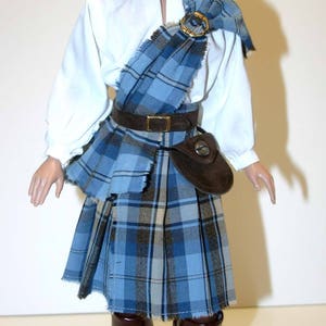 May include: A doll wearing a blue and white plaid kilt, a white shirt, a brown belt, a brown hat, and brown boots.