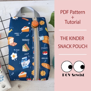 May include: A navy blue snack pouch with a handle, featuring a colorful food-themed pattern of eggs, sandwiches, and cake. The pouch has a zipper and a burger-shaped charm. Text on the pouch includes "CARROT CAKE" and "MILK". The text "PDF Pattern + Tutorial" is also visible.