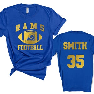 May include: A blue t-shirt with gold lettering and graphics. The front of the shirt displays the words "RAMS FOOTBALL" with a football graphic. The back of the shirt has the name "SMITH" and the number "35".