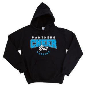 Puede incluir: Sudadera con capucha negra con el texto "PANTHERS CHEER Dad SABRINA" en blanco y azul. La sudadera tiene un bolsillo delantero y una capucha con cordón. El texto está en una fuente de estilo universitario.