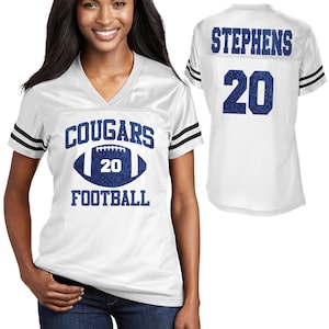 May include: White football jersey with blue text and graphics. The front of the jersey reads "COUGARS FOOTBALL" with a football graphic and the number "20". The back of the jersey displays the name "STEPHENS" and the number "20".