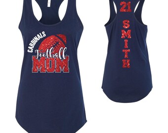 May include: Navy blue vest top with a football design. The front features the words "Cardinals Football MOM" with a red glitter football graphic. The back displays "21 SMITH" in red glitter.