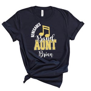May include: A navy blue short-sleeve t-shirt featuring a yellow musical note icon and white and yellow text that reads RENEGADES BAND AUNT Brian. The shirt has a crew neckline and is tied in a knot at the bottom hem, displaying a graphic print.