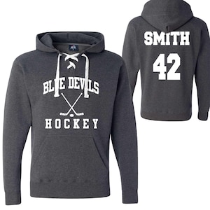 Può includere: Felpa con cappuccio grigio antracite con testo bianco "BLUE DEVILS HOCKEY" e bastoni da hockey incrociati. Il retro della felpa mostra "SMITH" e il numero "42" in bianco.