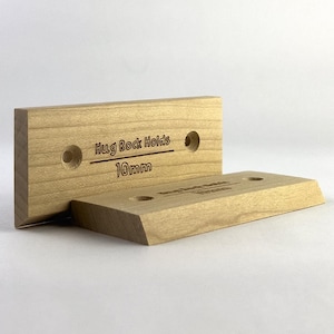 Puede incluir: Un soporte de pared de madera para agarres de escalada, etiquetado como "Hug Rock Holds 10mm".