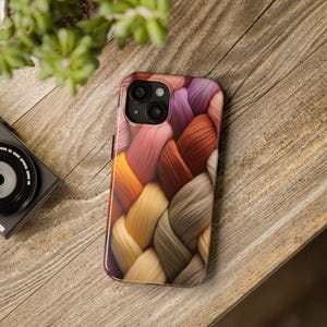 May include: A phone case with a braided pattern in shades of brown, orange, yellow, and purple. The case has a raised camera bump with three lenses.