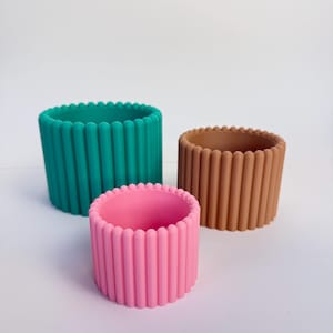 May include: Three silicone planters in different sizes and colors: teal, brown, and pink. The planters have a ribbed design.
