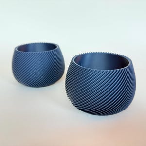May include: Two small, dark blue, ceramic planters with a spiral pattern. The planters are empty and sitting on a white surface.