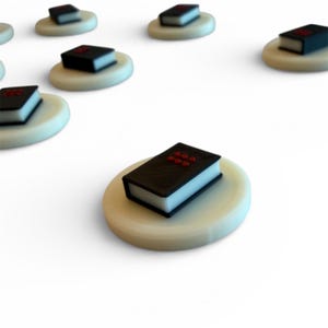 Puede incluir: Una colección de pequeños objetos negros con forma de libro y detalles rojos, colocados sobre plataformas circulares de color blanquecino. Los libros tienen bordes blancos y están dispuestos sobre un fondo blanco. Los objetos parecen modelos en miniatura.