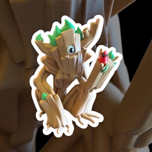 Peut inclure: Figurine imprimée en 3D d'un personnage de dessin animé en forme d'arbre, avec un corps brun clair et des accents verts sur la tête et les mains. Le personnage tient un petit oiseau rouge avec des feuilles vertes. La figurine a un contour blanc.
