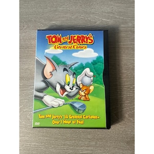 Może przedstawiać: Pudełko DVD z "Tom and Jerry's Greatest Chases". Okładka przedstawia kota Toma i mysz Jerry'ego grających w golfa na zielonym polu. Tytuł jest w kolorze żółtym i czerwonym, z tekstem "Tom and Jerry's 14 Greatest Cartoons - Over 1 Hour of Fun!"