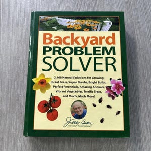 May include: A gardening book titled "Backyard Problem Solver" with a green border. The cover displays the title in orange and green, alongside illustrations of flowers, tomatoes, and a portrait of Jerry Baker.