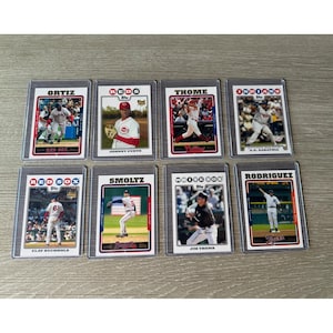 Puede incluir: Ocho tarjetas de béisbol coleccionables, cada una en una funda protectora. Las tarjetas muestran a jugadores de béisbol en acción, con logotipos de equipos y nombres de jugadores. Las tarjetas están dispuestas sobre una superficie clara.