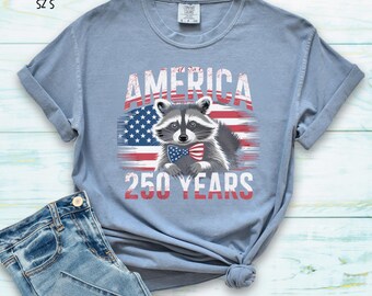Camiseta de algodón con motivo del 250 aniversario de Estados Unidos, diseño de mapache con colores cómodos y bandera estadounidense.