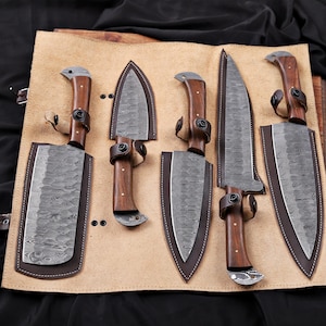 Op de afbeelding: Een set van zes messen met houten handvatten en patronen op de bladen, gepresenteerd op een bruinleren rol. Elk mes heeft een leren schede en een donkerbruin handvat. De bladen hebben een uniek, getextureerd patroon.