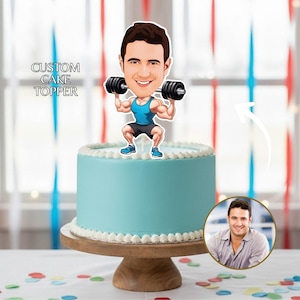 May include: A light blue cake with white frosting and a cartoon cake topper of a man lifting weights. The cake is on a wooden cake stand. The words "CUSTOM CAKE TOPPER" are in the upper left corner. A photo of the man is in the lower right corner.