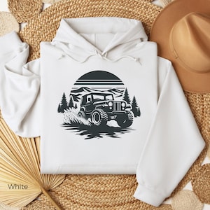May include: White hooded sweatshirt featuring a black and white graphic of a jeep driving through a mountain landscape with a sunset in the background.