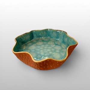 May include: A ceramic bowl with a distinctive design. The interior is glazed turquoise with a bubble pattern, contrasting with the textured, reddish-brown exterior. The bowl's rim has a wavy, organic shape. A decorative piece for the home.