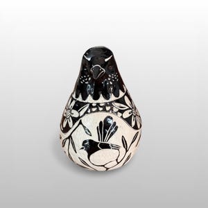 May include: A decorative ceramic bird ornament in black and white. The bird-shaped figurine features a black head and a body decorated with a bird and floral design. The item is a handcrafted piece.